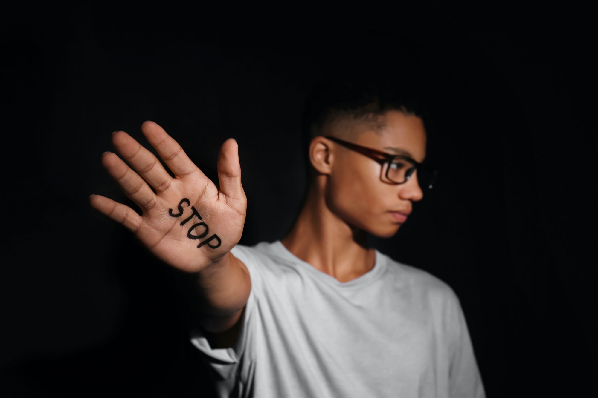 African-American teenage boy with word STOP written on hand against dark background